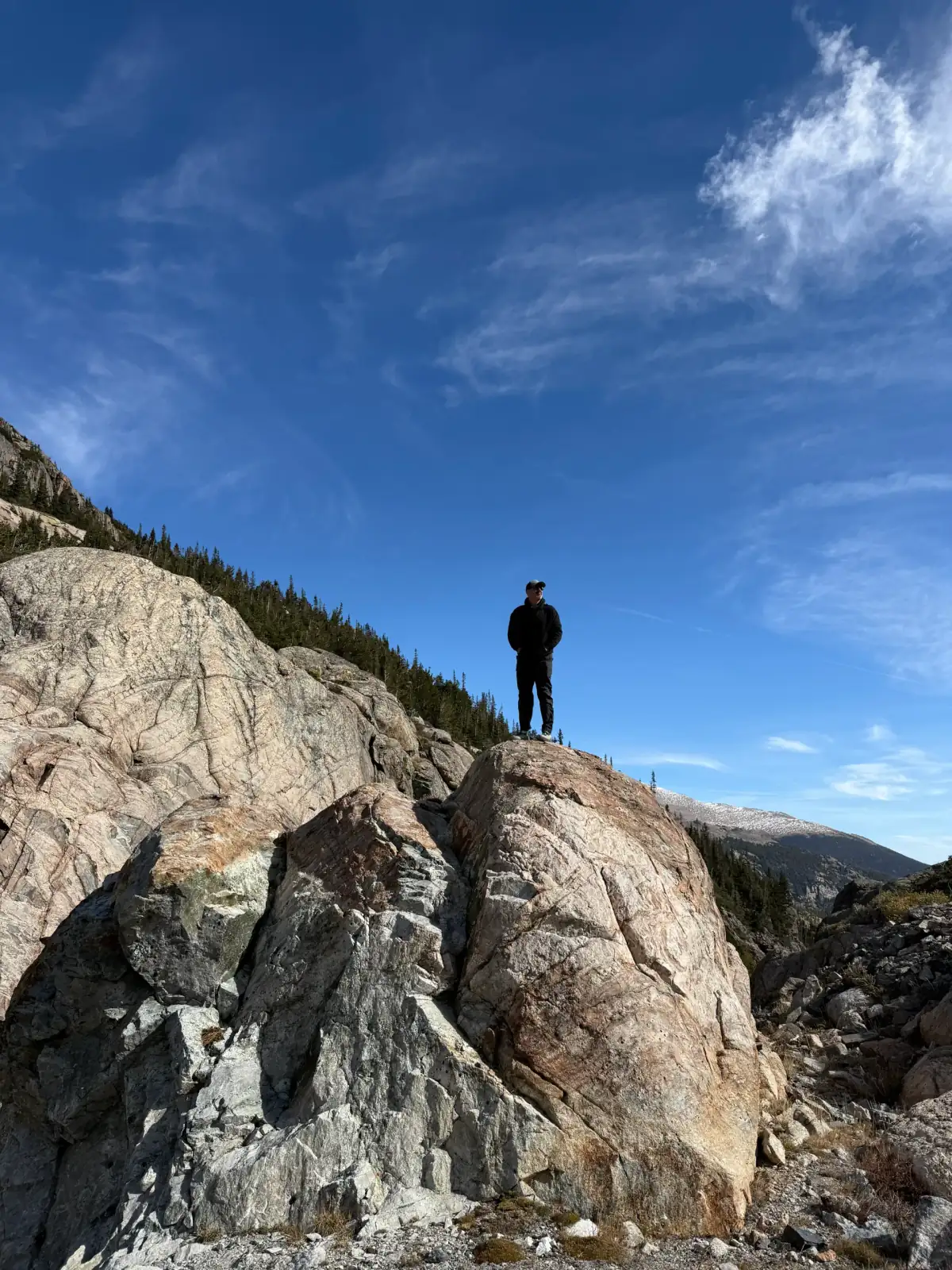 A lone hiker standing on a rocky mountain summit beneath a wide blue sky